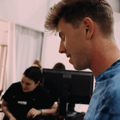 A Man In A Blue Shirt Looks At A Computer Screen GIF