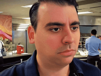 A Man In A Blue Shirt Looks At The Camera With A Red Ketchup Dispenser In The Background GIF