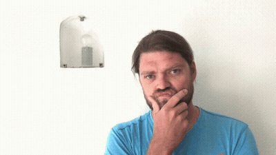 A Man In A Blue Shirt Points Up At A Light Bulb On A Wall GIF