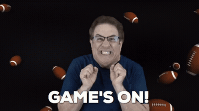 A Man In A Blue Shirt Says Game 'S On With Footballs Flying Around Him GIF