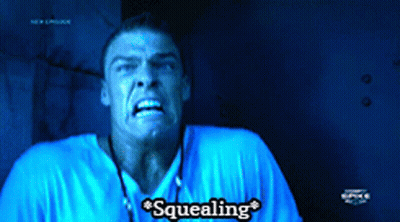A Man In A Blue Shirt Says Squealing In A Dark Room GIF