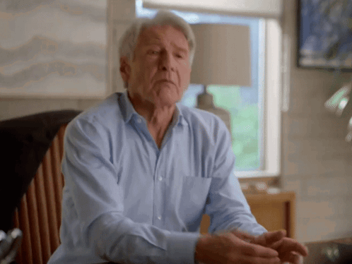 A Man In A Blue Shirt Sits In A Chair GIF