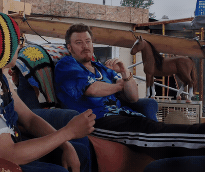 A Man In A Blue Shirt Sits On A Couch With A Woman In A Crocheted Hat GIF