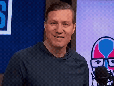 A Man In A Blue Shirt Stands In Front Of A Microphone In Front Of A Sign That Says S GIF