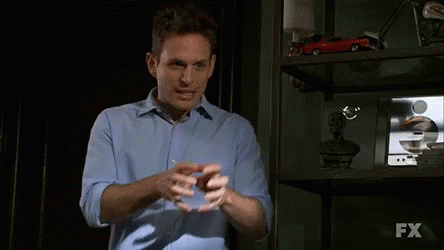 A Man In A Blue Shirt Stands In Front Of A Shelf With Fx Written On It GIF