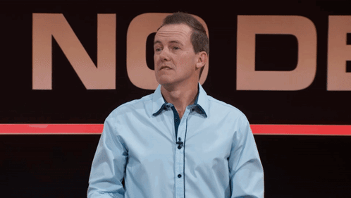 A Man In A Blue Shirt Stands In Front Of A Sign That Says No De GIF