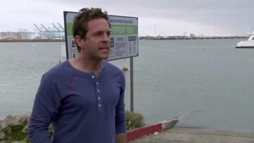 A Man In A Blue Shirt Stands In Front Of A Sign That Says Notice GIF