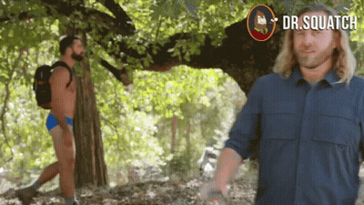 A Man In A Blue Shirt Stands In Front Of A Tree With Dr.squatch Written On The Bottom Right GIF