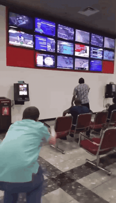 A Man In A Blue Shirt Stands In Front Of A Wall With Lots Of Tv Screens GIF