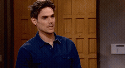 A Man In A Blue Shirt Stands In Front Of A Wooden Door GIF