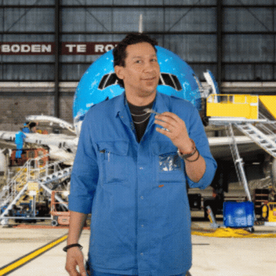 A Man In A Blue Shirt Stands In Front Of An Airplane In A Hangar With Boden Te Ro Written On The Wall Behind Him GIF