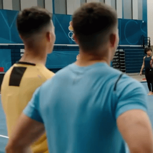 A Man In A Blue Shirt Stands Next To A Man In A Yellow Shirt GIF