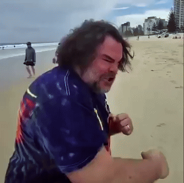 A Man In A Blue Shirt Stands On A Beach GIF