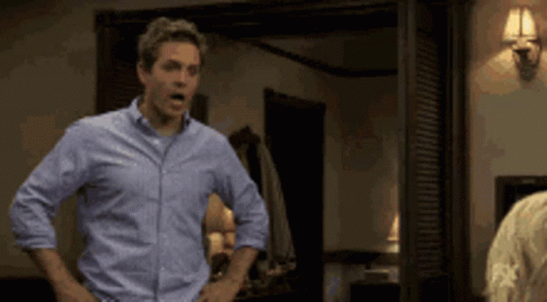 A Man In A Blue Shirt Stands With His Hands On His Hips GIF