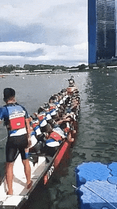 A Man In A Blue Shirt That Says ' Singapore ' On It Is Rowing A Boat GIF