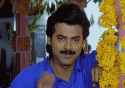 A Man In A Blue Shirt With A Mustache Is Standing In Front Of Flowers GIF