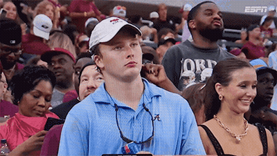 A Man In A Blue Shirt With The Letter A On It Sits In A Crowd GIF