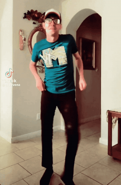 A Man In A Blue Shirt With The Letter M On It Is Dancing In A Hallway GIF