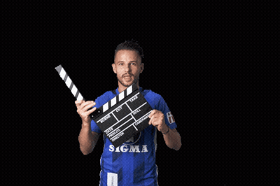 A Man In A Blue Sigma Shirt Is Holding A Clapper Board GIF