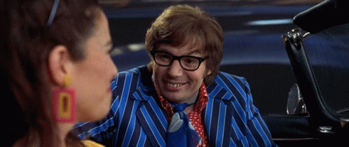 A Man In A Blue Striped Suit And Tie Is Talking To A Woman Wearing Earrings That Say 0 GIF