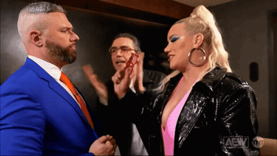 A Man In A Blue Suit And A Woman In A Pink Top Are Standing Next To Each Other In A Room . GIF
