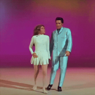 A Man In A Blue Suit And A Woman In A White Dress Are Dancing Together GIF