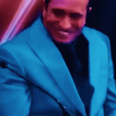 A Man In A Blue Suit And Black Tie Is Smiling While Holding A Microphone . GIF