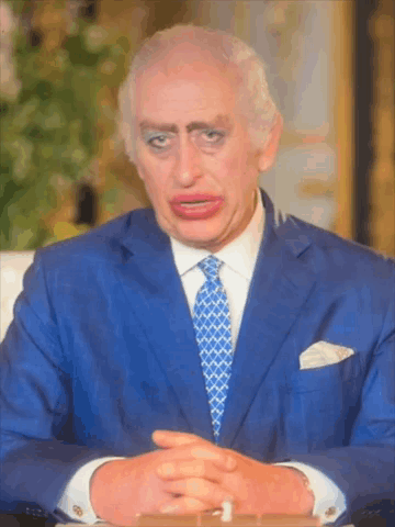 A Man In A Blue Suit And Tie Is Sitting At A Table GIF