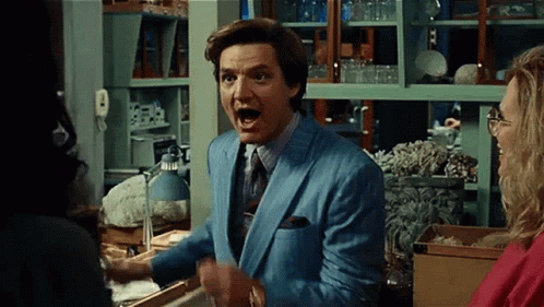 A Man In A Blue Suit And Tie Is Standing In Front Of A Woman In A Room . GIF