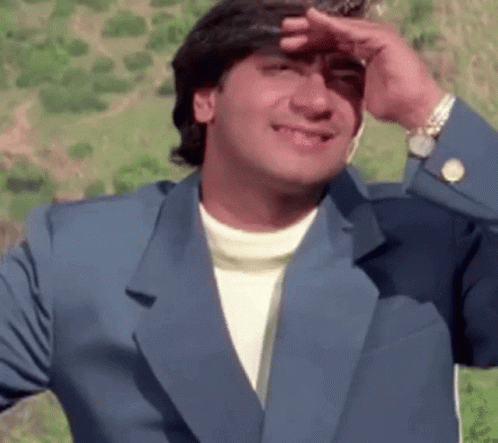 A Man In A Blue Suit Is Covering His Face With His Hand And Smiling . GIF