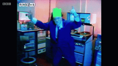 A Man In A Blue Suit Is Dancing In Front Of A Sign That Says Bbc V1 GIF