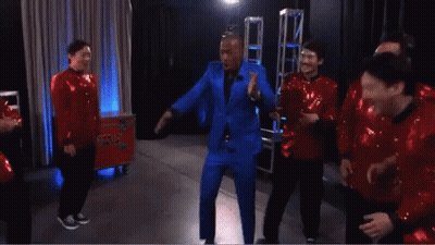 A Man In A Blue Suit Is Dancing With A Group Of Men In Red Sequins GIF