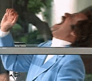 A Man In A Blue Suit Is Looking Out A Window With His Hands In The Air . GIF