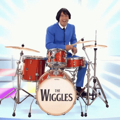 A Man In A Blue Suit Is Playing A Drum Set That Says The Wiggles On It GIF