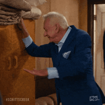 A Man In A Blue Suit Is Reaching For Something On A Wall .. GIF