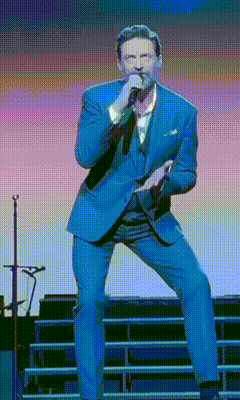 A Man In A Blue Suit Is Singing Into A Microphone On Stage GIF
