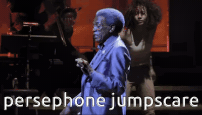 A Man In A Blue Suit Is Singing Into A Microphone With The Words Persephone Jumpscare Behind Him GIF