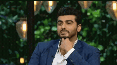 A Man In A Blue Suit Is Sitting In Front Of A Green Background With His Hand On His Chin . GIF