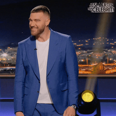 A Man In A Blue Suit Is Smiling In Front Of A Sign That Says " And Smarter Than Celebrity " GIF
