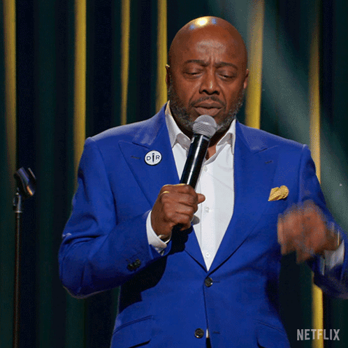 A Man In A Blue Suit Is Speaking Into A Microphone With A Netflix Logo In The Corner GIF