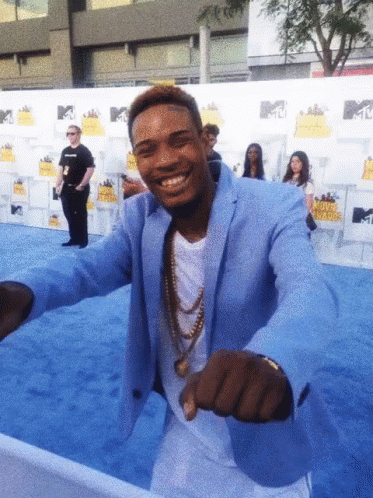 A Man In A Blue Suit Is Standing On A Blue Carpet At A Movie Awards Event GIF