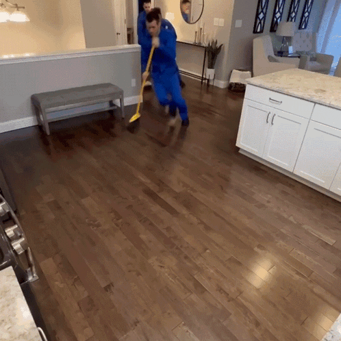 A Man In A Blue Suit Is Sweeping The Floor In A Kitchen GIF