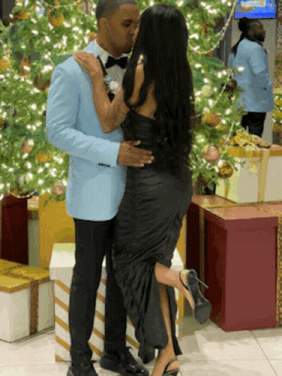 A Man In A Blue Suit Kisses A Woman In A Black Dress In Front Of A Christmas Tree GIF