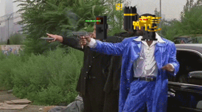 A Man In A Blue Suit Points A Gun At Another Man In A Black Suit GIF