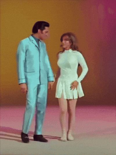 A Man In A Blue Suit Stands Next To A Woman In A White Skirt GIF