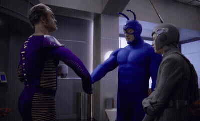 A Man In A Blue Superhero Costume Is Shaking Hands With Two Other Men GIF