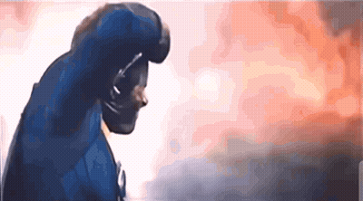 A Man In A Blue Superhero Costume Is Standing In Front Of A Burning Building GIF