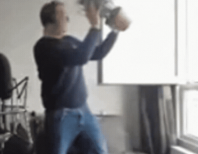 A Man In A Blue Sweater And Blue Jeans Is Holding A Bucket In His Hands . GIF
