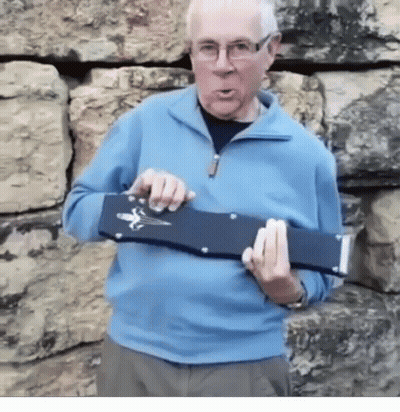 A Man In A Blue Sweater And Glasses Is Holding A Black Object In His Hands GIF