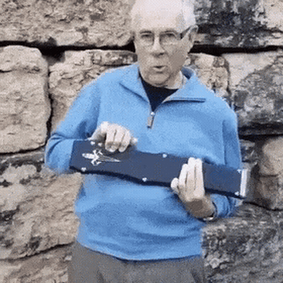 A Man In A Blue Sweater And Glasses Is Holding A Blue Object In His Hands . GIF